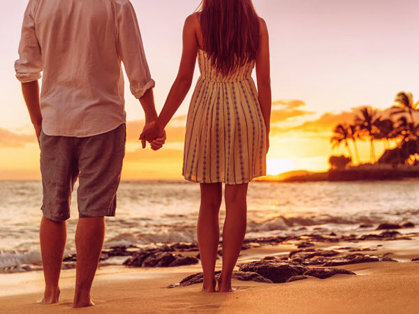 Couple walking hand in hand along a sunset lit beach